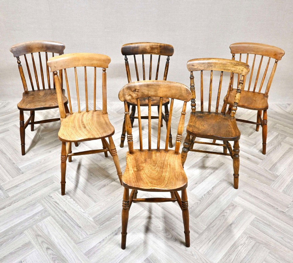 A set of six antique wooden country kitchen chairs featuring spindle backs, curved top rails, turned legs, and contoured wooden seats.