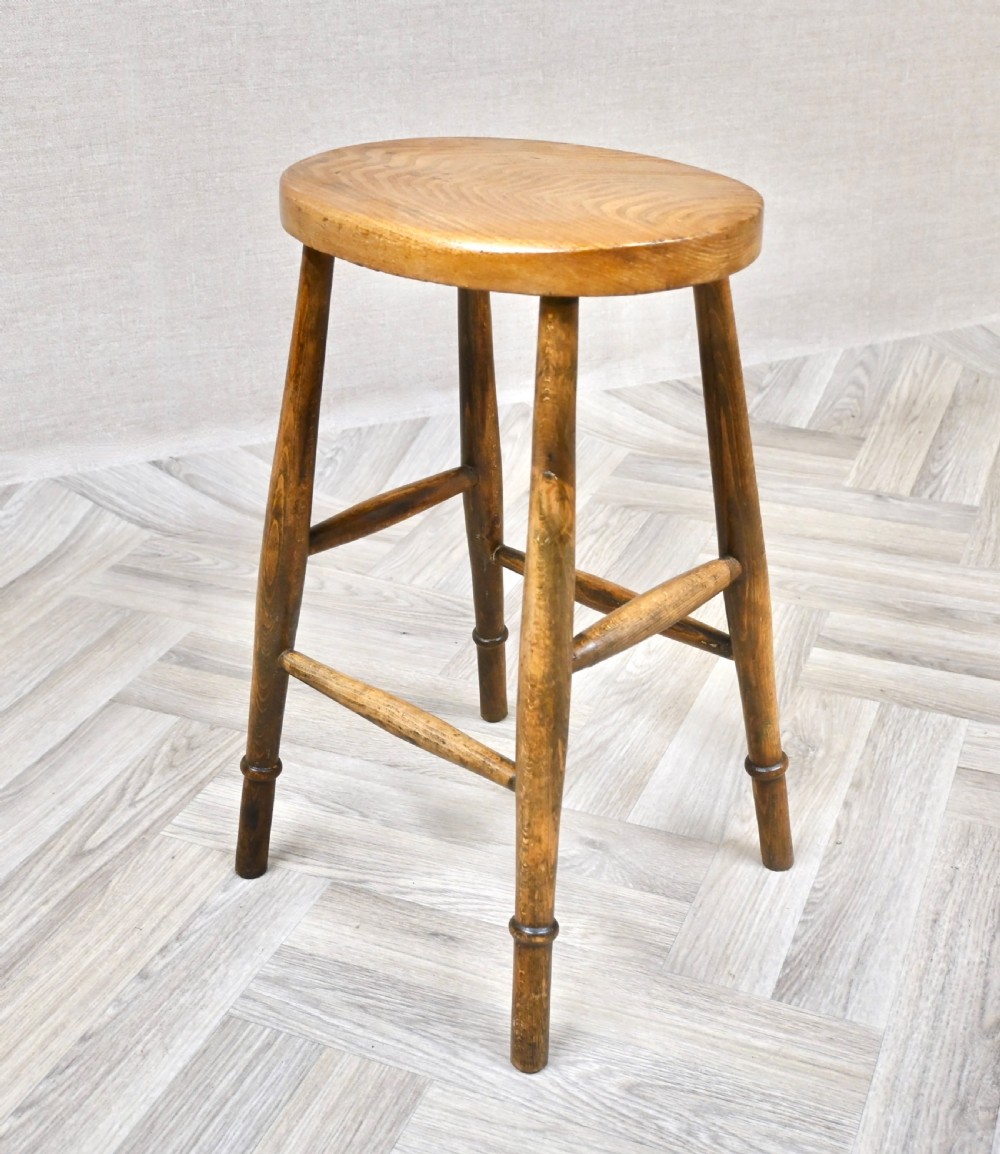A 19th-century rustic wooden country stool with four turned legs, supportive stretchers, and a thick oval seat displaying visible wood grain.