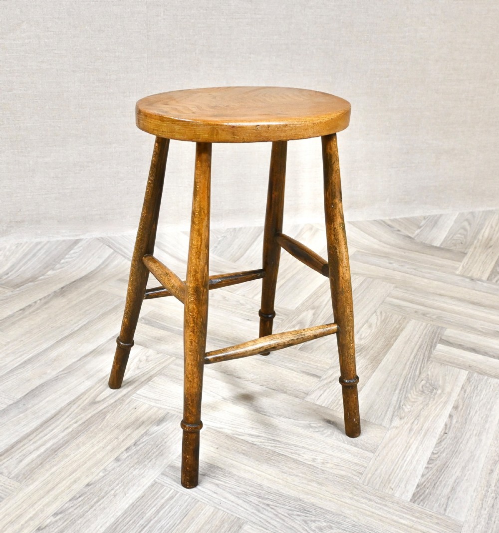 A 19th-century rustic wooden country stool with four turned legs, supportive stretchers, and a thick oval seat displaying visible wood grain. View II