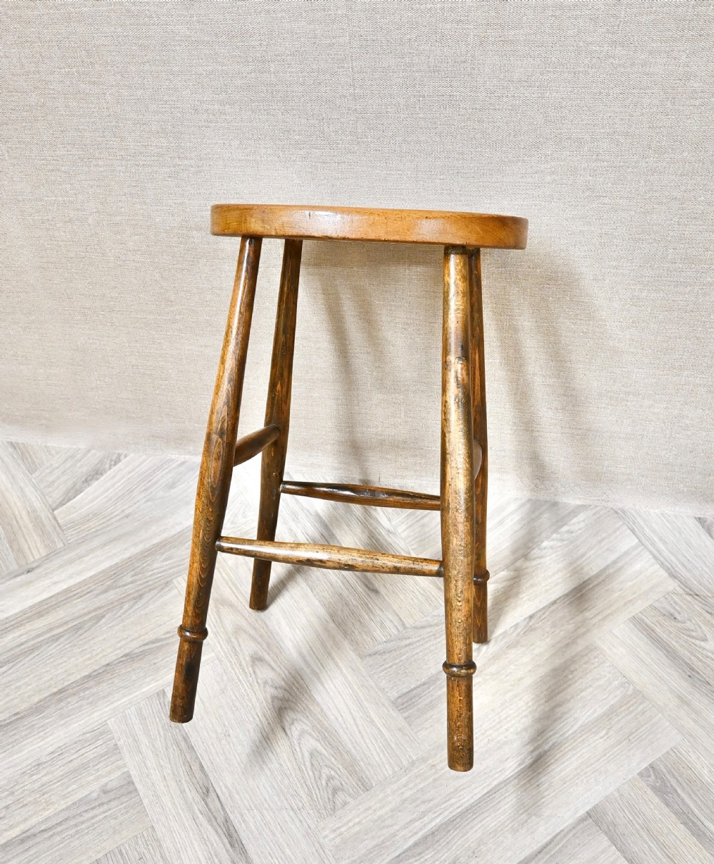 A 19th-century rustic wooden country stool with four turned legs, supportive stretchers, and a thick oval seat displaying visible wood grain. View III