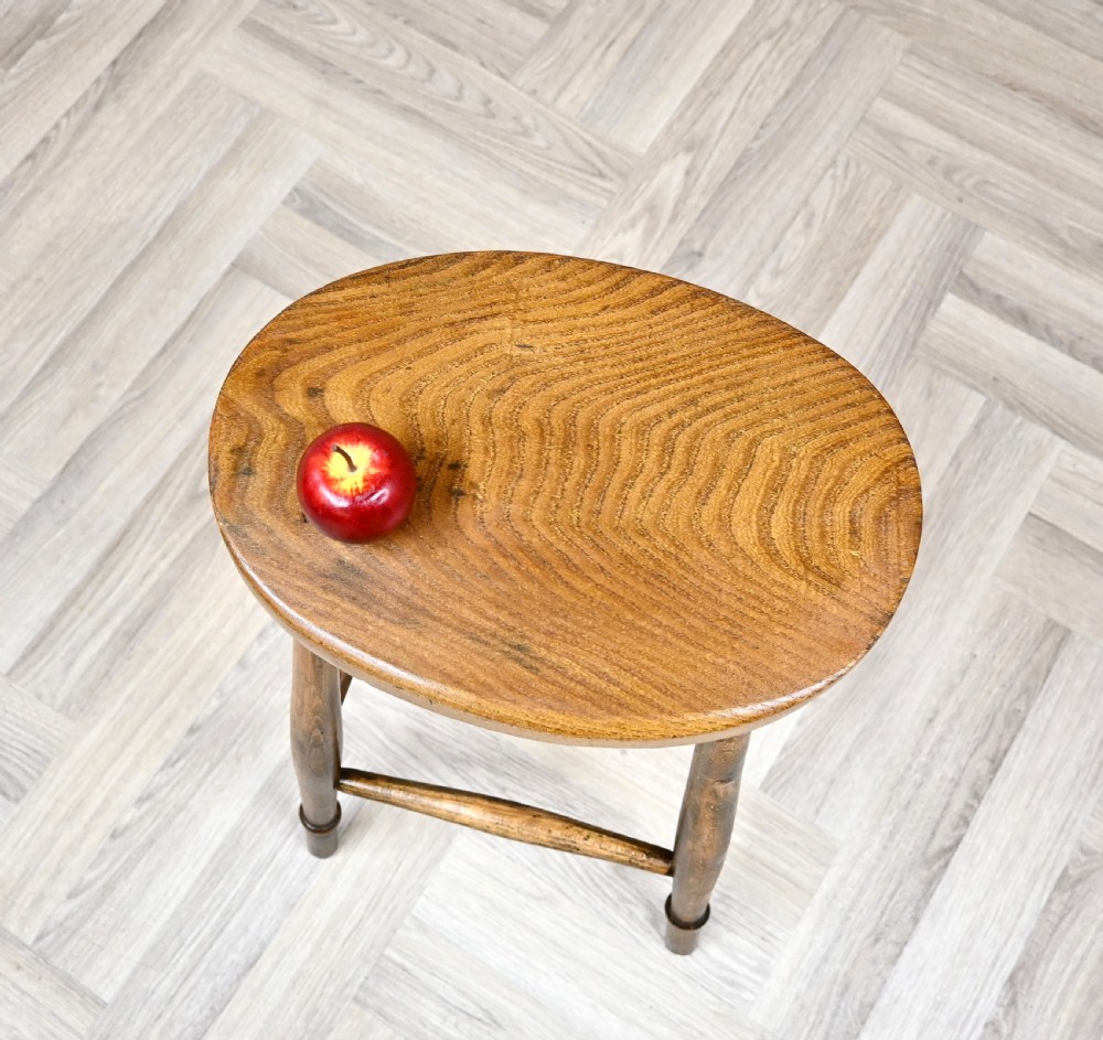 A 19th-century rustic wooden country stool with four turned legs, supportive stretchers, and a thick oval seat displaying visible wood grain. View IV