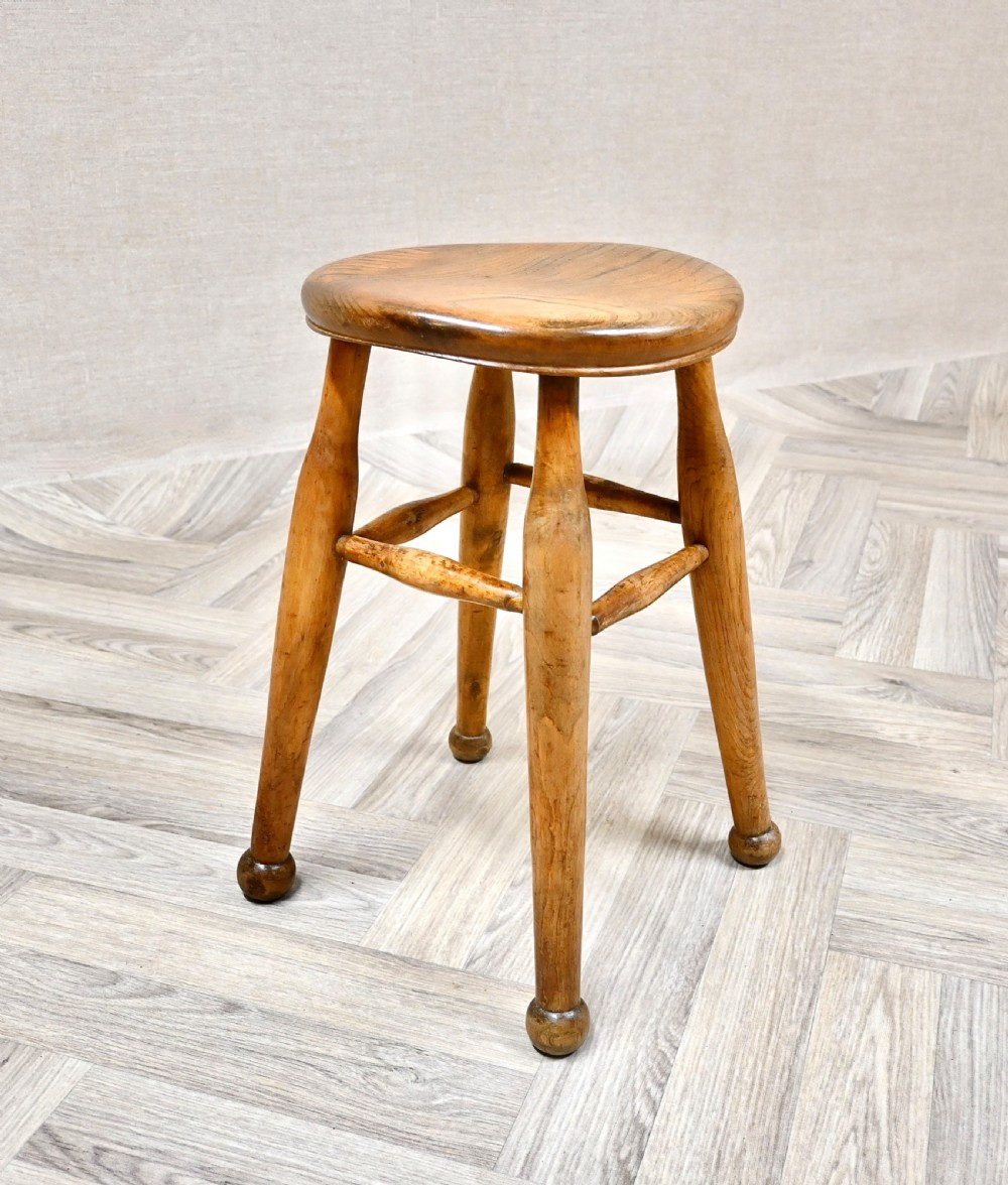 A 19th-century rustic wooden stool featuring a contoured round seat, splayed turned legs ending in ball feet, and turned stretchers. View II