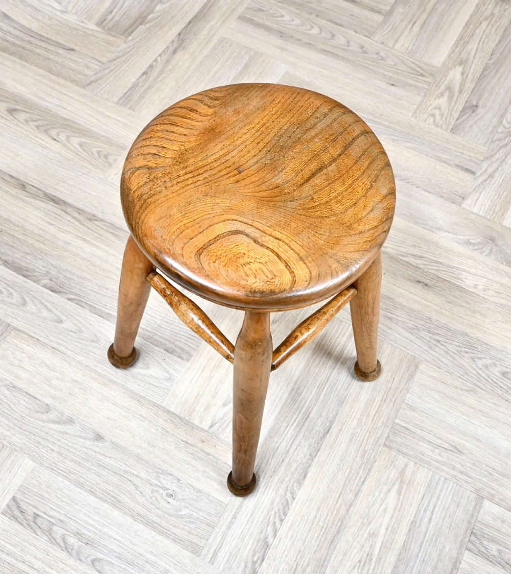 A 19th-century rustic wooden stool featuring a contoured round seat, splayed turned legs ending in ball feet, and turned stretchers. View III