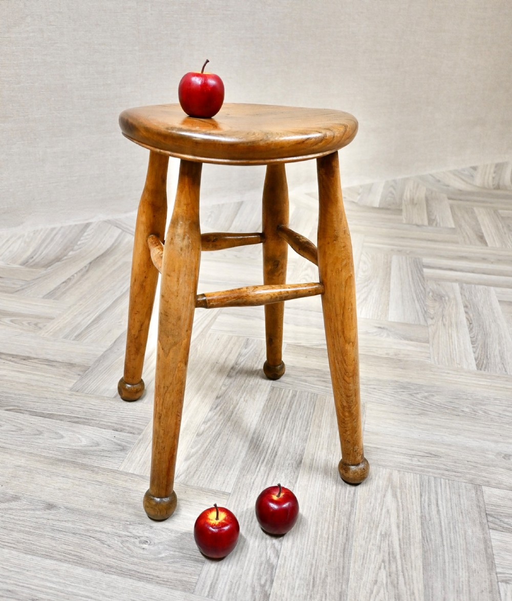 A 19th-century rustic wooden stool featuring a contoured round seat, splayed turned legs ending in ball feet, and turned stretchers. View V