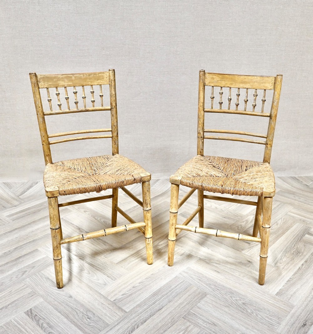A pair of antique painted bamboo side chairs featuring turned spindle backrests and woven rush seats.