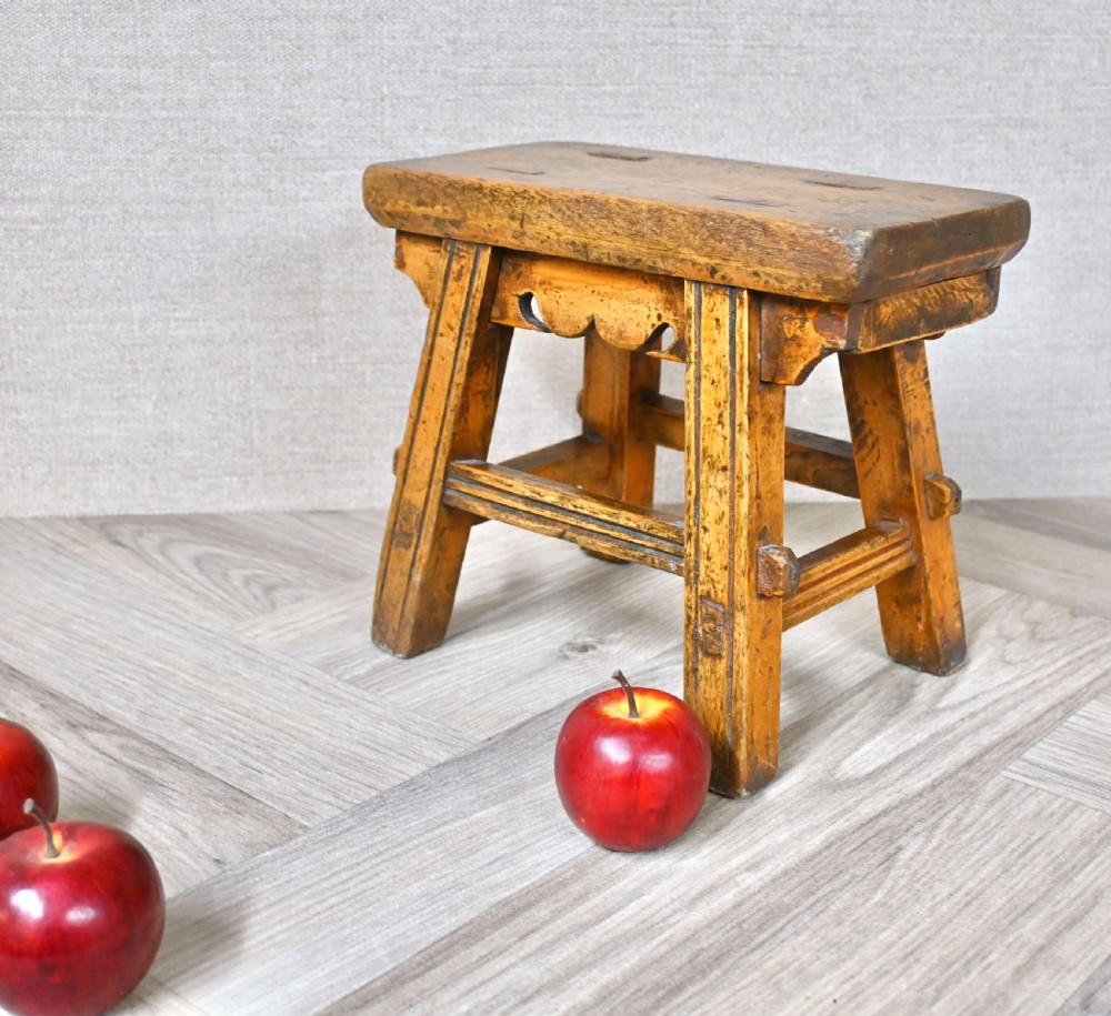 A small 19th-century rustic wooden stool featuring carved splayed legs, mortise and tenon joinery, and a weathered brown timber finish. View V