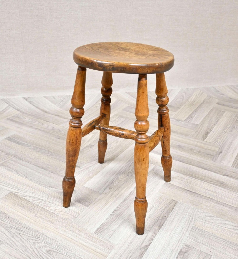 A 19th-century wooden Windsor stool featuring a circular solid seat, four turned legs, and H-frame stretchers.