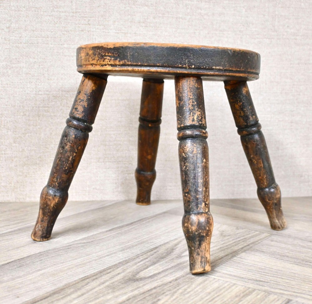 A nineteenth-century round wooden hearth stool with four thick turned legs and a distressed dark brown painted finish. View II