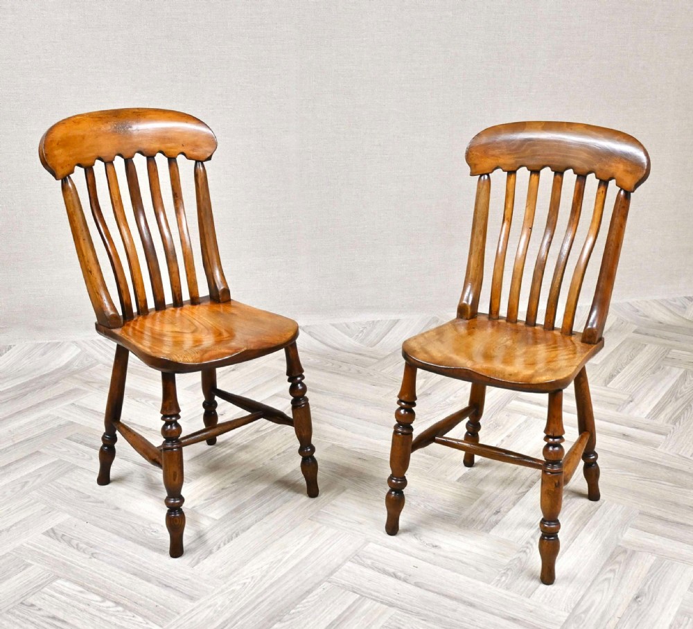 A pair of antique wooden Windsor chairs featuring vertical lath backs, shaped saddle seats, and turned legs joined by H-stretchers.