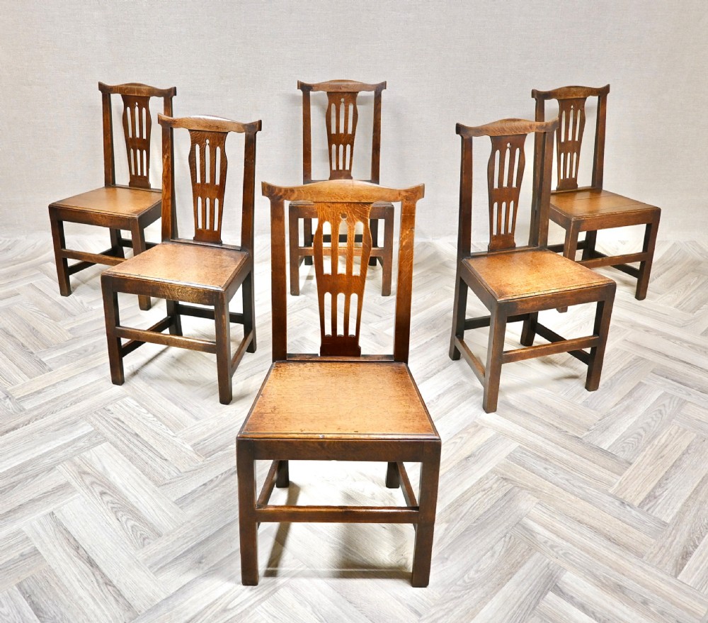 A set of six Georgian oak country dining chairs featuring pierced back splats, flat wooden seats, and sturdy stretchered legs.