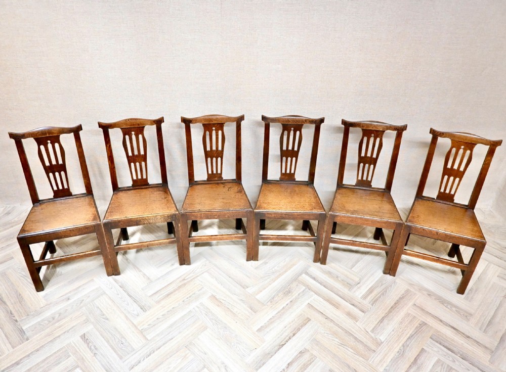 A set of six Georgian oak country dining chairs featuring pierced back splats, flat wooden seats, and sturdy stretchered legs. View III