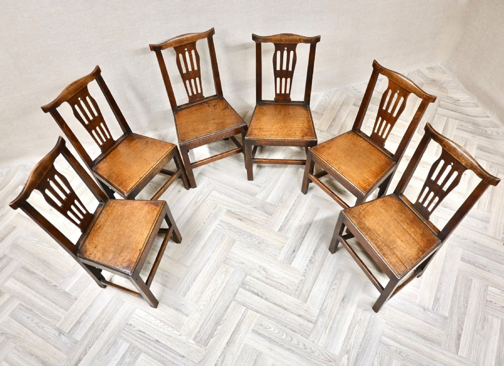 A set of six Georgian oak country dining chairs featuring pierced back splats, flat wooden seats, and sturdy stretchered legs. View IV