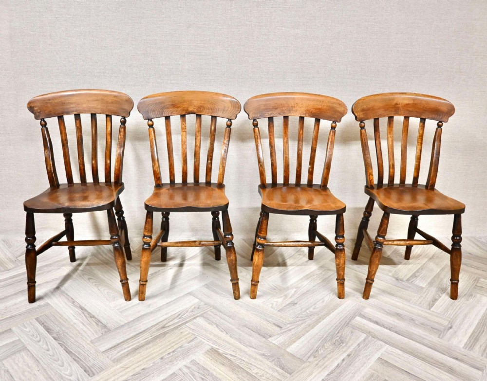 A set of four antique wooden Windsor lathback dining chairs featuring curved top rails, vertical slats, contoured saddle seats, and turned legs with stretchers.