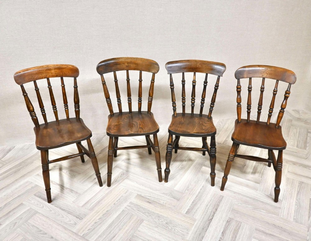 Set of four antique dark brown wood Windsor dining chairs featuring spindle backrests, shaped wooden seats, and turned legs.