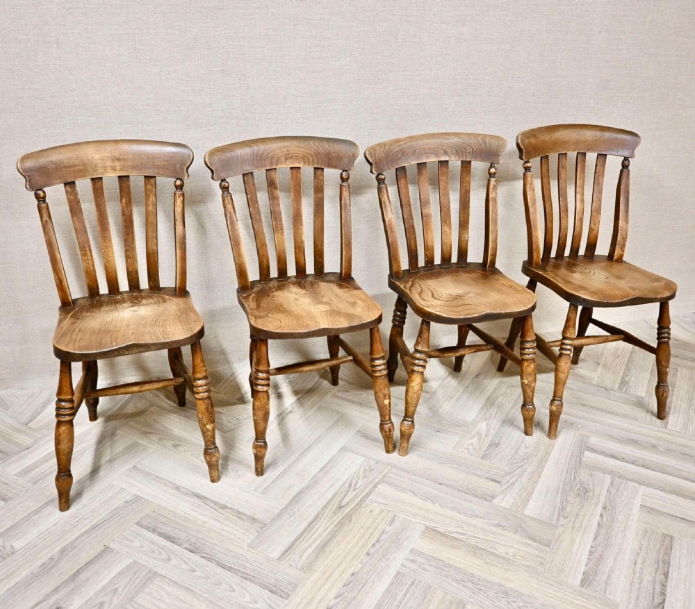 A set of four antique wooden Windsor layback kitchen chairs featuring contoured saddle seats, vertical back slats, turned front legs, and a rich warm brown timber finish.