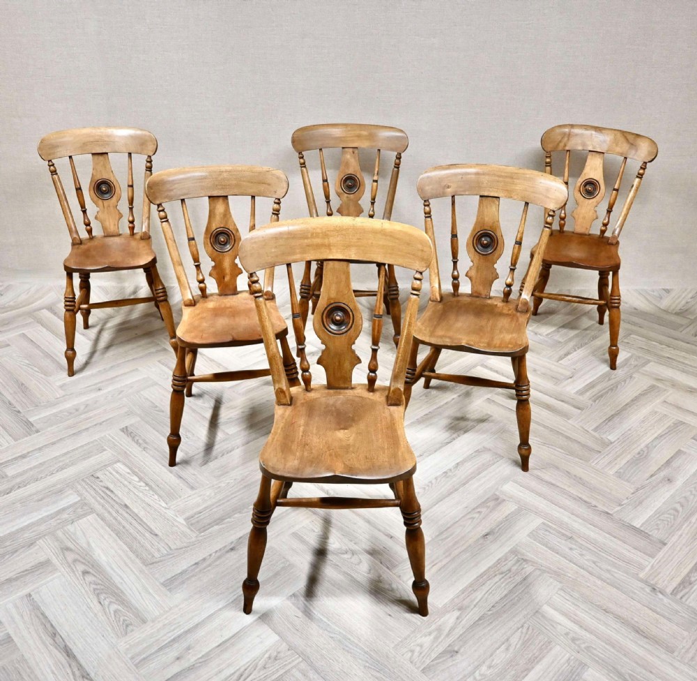 A matching set of six antique warm brown wooden Windsor kitchen chairs featuring carved bullseye central splats and turned legs.