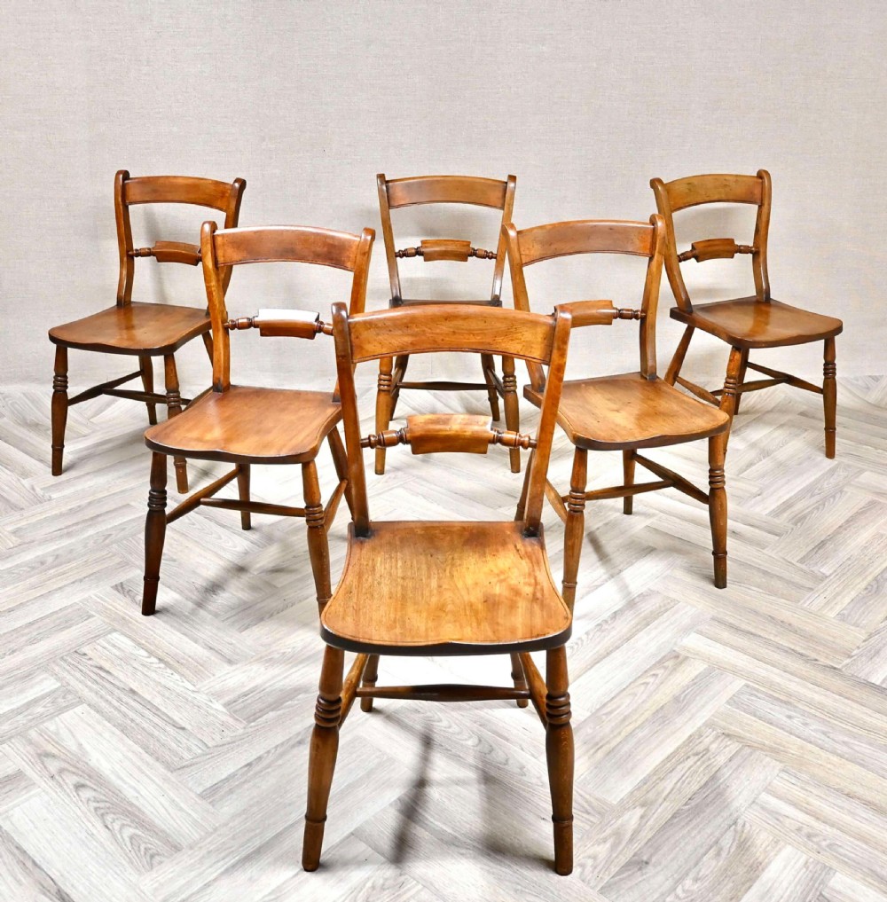 A set of six matching antique wooden barback Windsor dining chairs with turned legs and contoured seats arranged on a parquet floor.