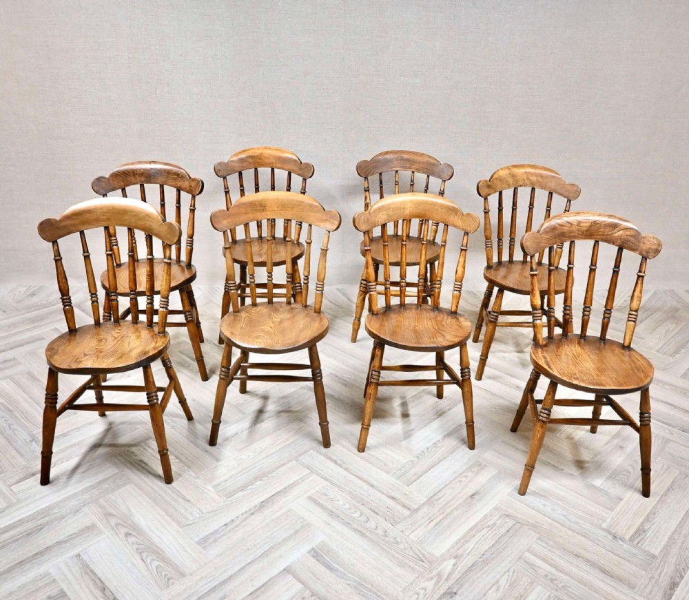 A set of eight wooden Windsor dining chairs featuring shaped cresting top rails, spindle backs, circular penny seats, and turned legs with stretchers.