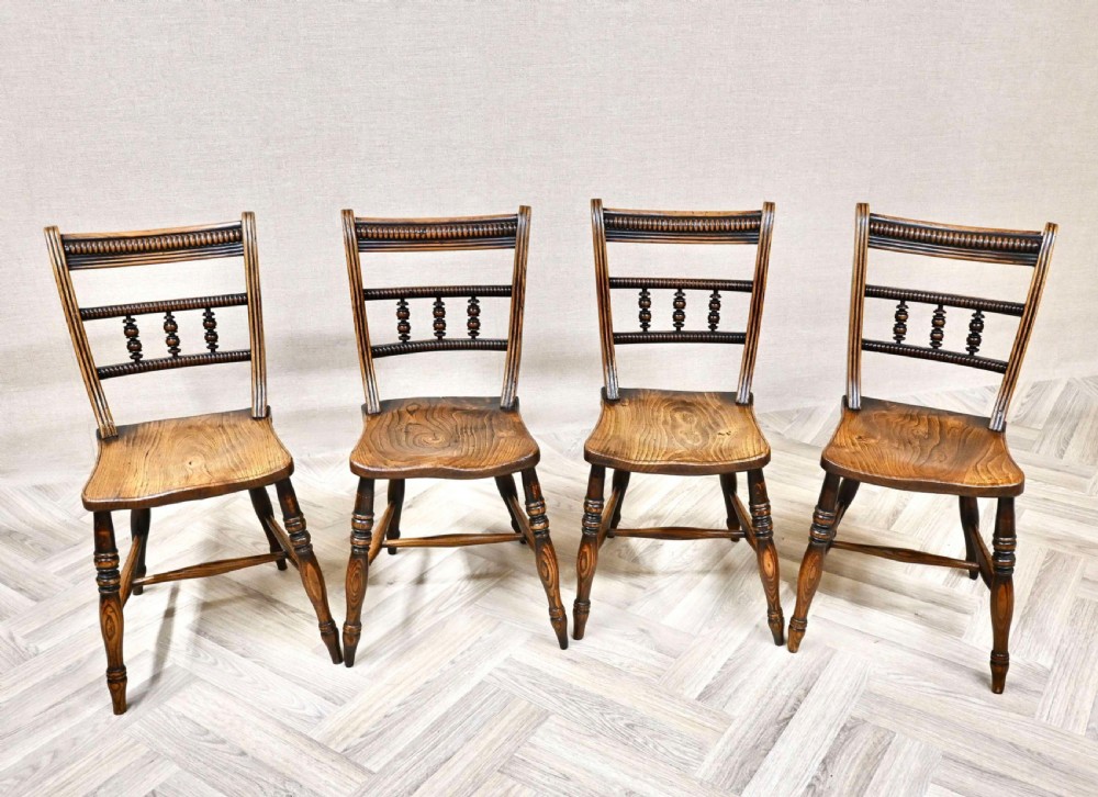 Set of four antique warm brown wooden Windsor dining chairs featuring turned barback spindles, contoured solid seats, and turned legs.
