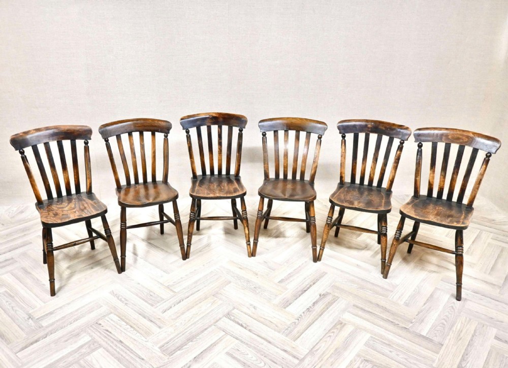 A set of six dark timber Windsor lathback kitchen chairs featuring shaped back rails, vertical slats, solid wooden seats, and turned legs.