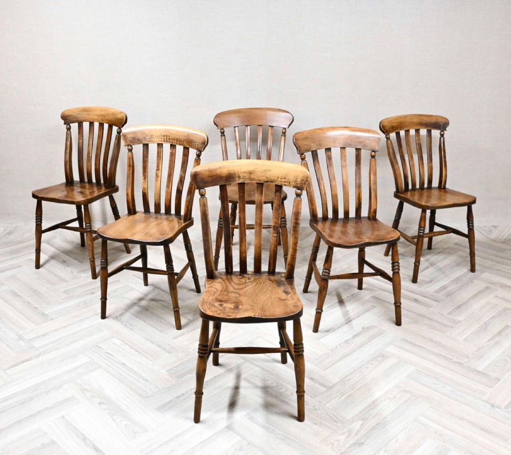A set of six matching antique wooden Windsor lathback kitchen chairs with contoured seats and turned legs arranged on a light parquet floor.