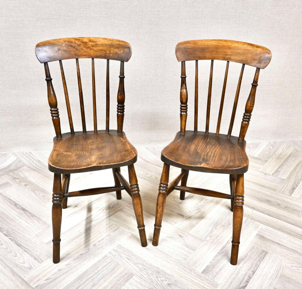 A pair of antique wooden Windsor stickback kitchen chairs featuring curved crest rails, vertical back spindles, shaped seats, and turned legs.