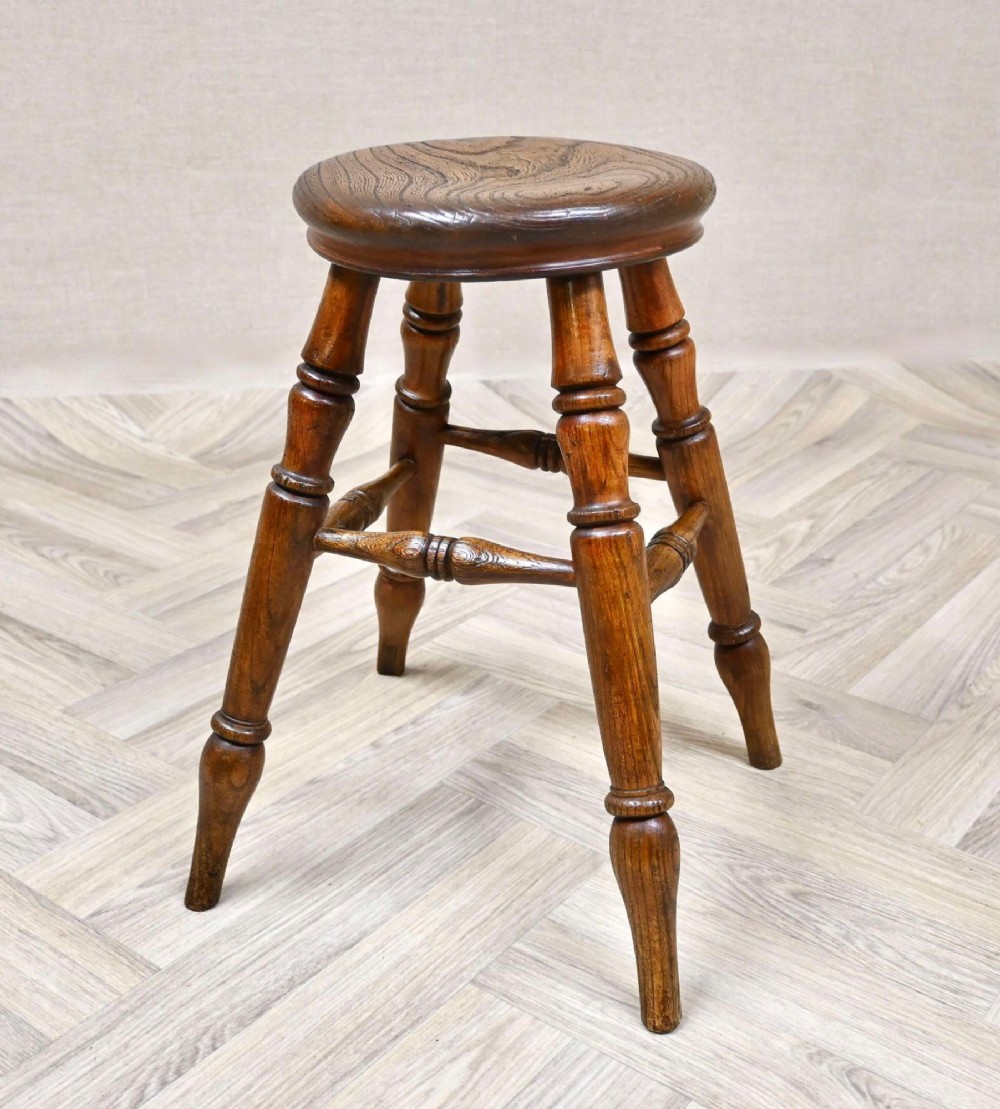 A nineteenth-century turned wooden Windsor stool featuring a circular polished seat supported by four splayed turned legs and turned stretchers.