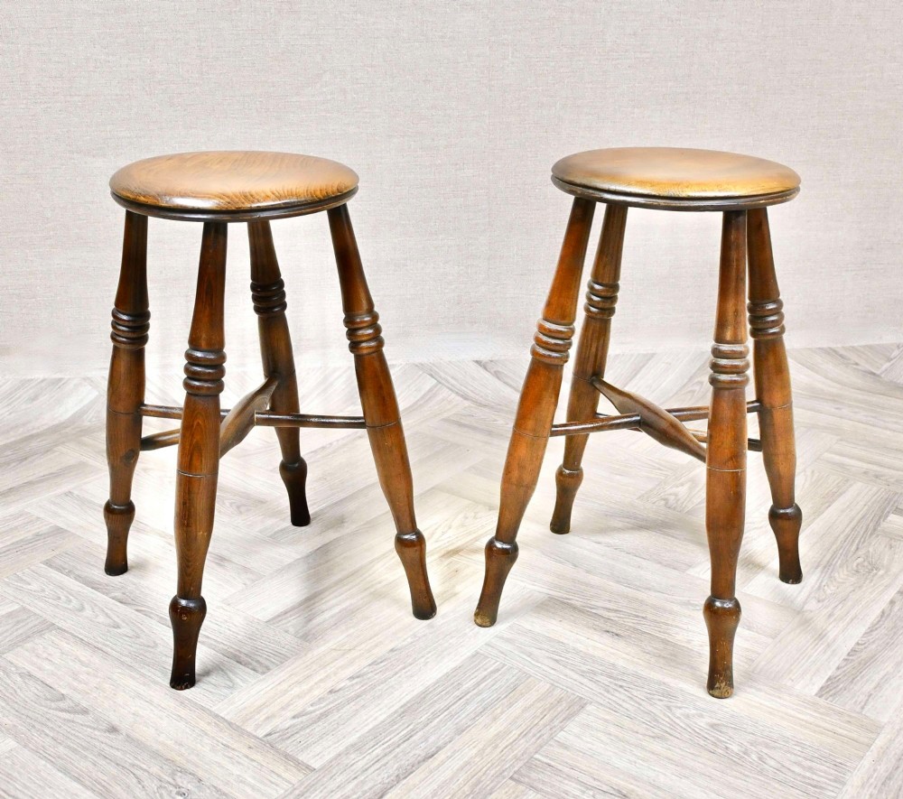 A pair of 19th-century turned wood Windsor stools with round seats, splayed legs, and cross stretchers.