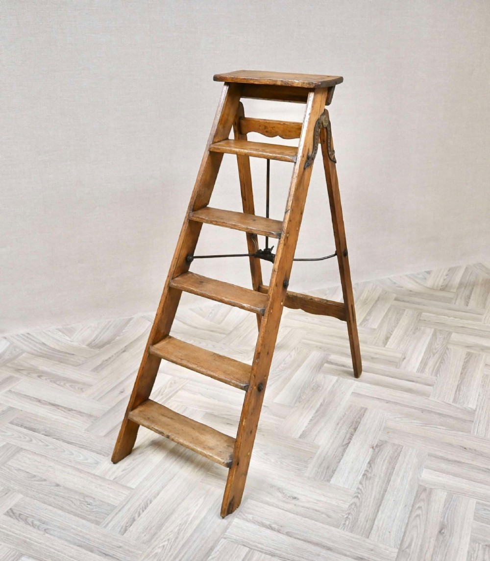 A vintage pine A-frame step ladder featuring wooden treads, iron side braces, and a top platform.