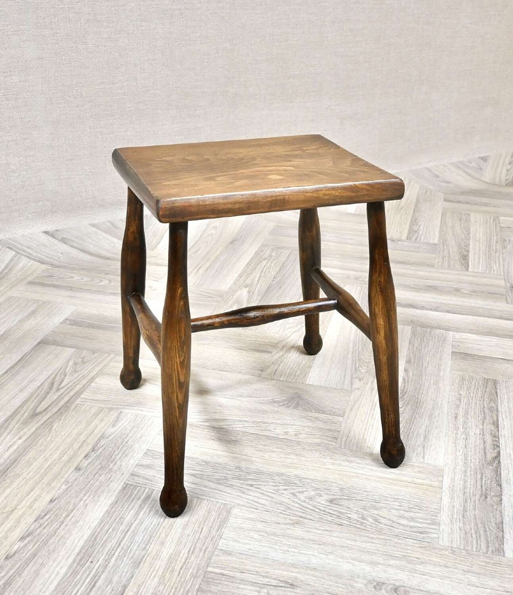 A small rectangular dark timber antique dairy stool featuring four turned legs joined by cross stretchers.