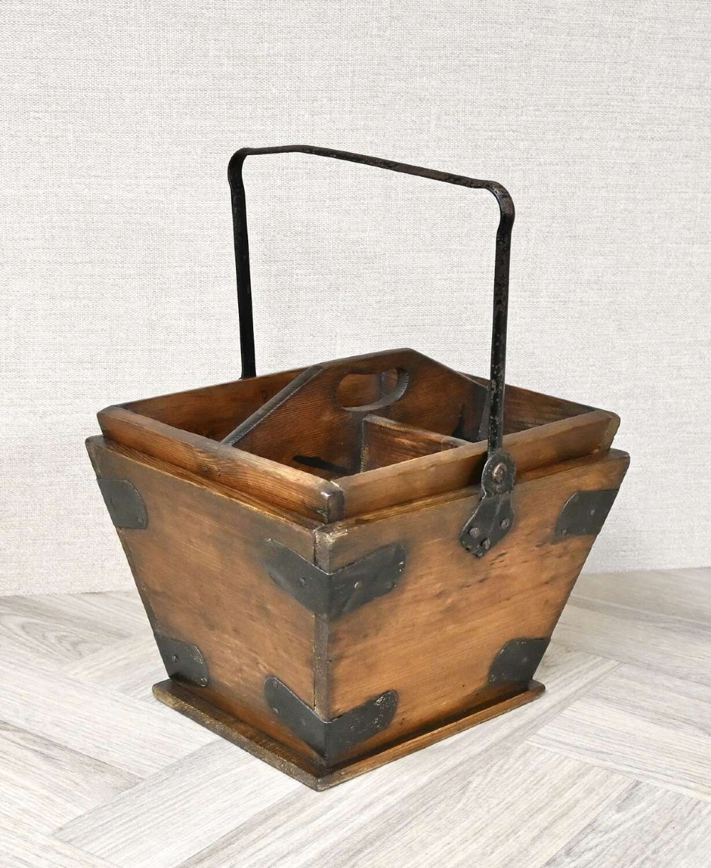 A tapered rectangular wooden housekeepers bucket with iron corner brackets, internal dividers, and a tall metal swing handle.
