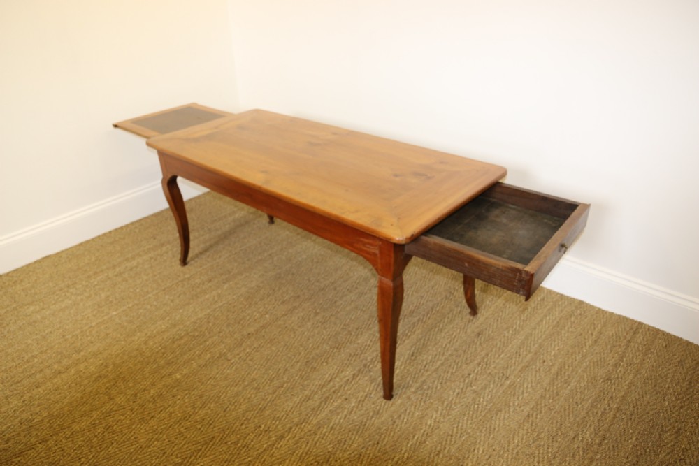 An antique French cherrywood farmhouse dining table featuring slender cabriole legs, an end drawer, and an extending pull-out slide.