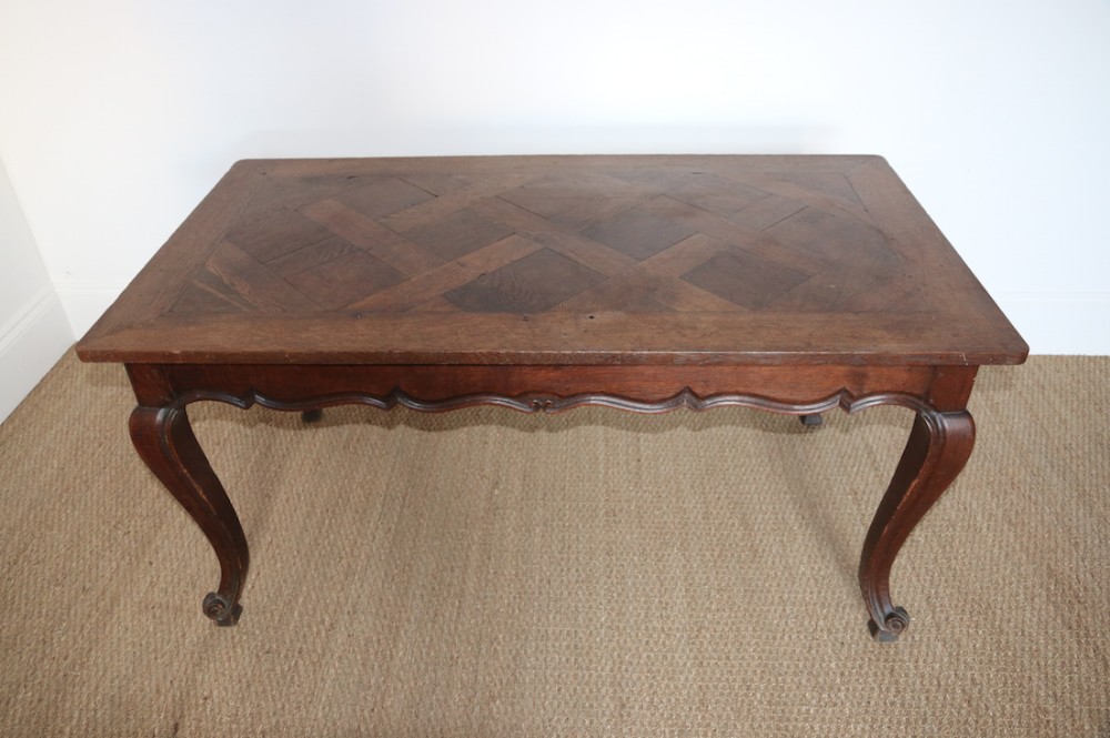 An eighteenth-century Louis XV style oak low table featuring a geometric parquet inlaid top, serpentine apron, and curved cabriole legs ending in scroll feet.