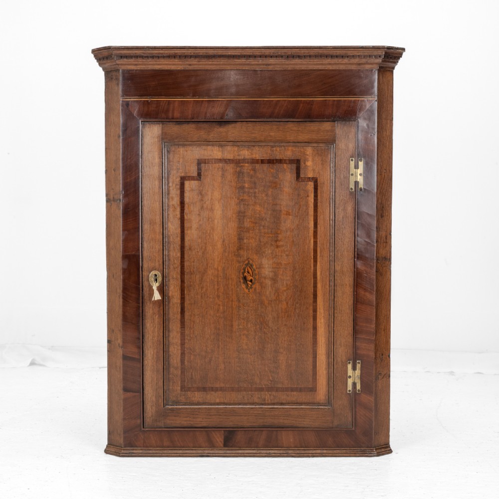 A late 18th-century Georgian oak wall-hanging corner cupboard featuring mahogany crossbanding, an inlaid central lozenge motif, a moulded top cornice, and brass H-hinges. View III