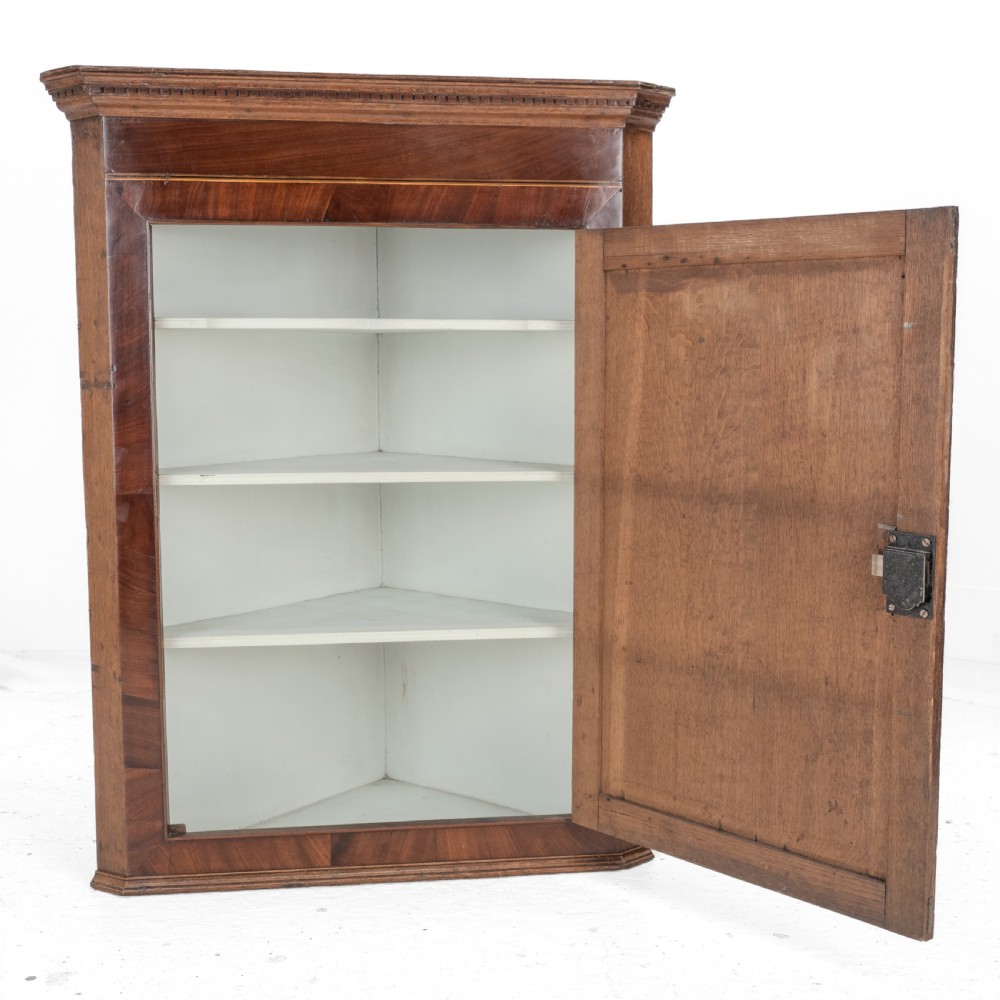 A late 18th-century Georgian oak wall-hanging corner cupboard featuring mahogany crossbanding, an inlaid central lozenge motif, a moulded top cornice, and brass H-hinges. View VI