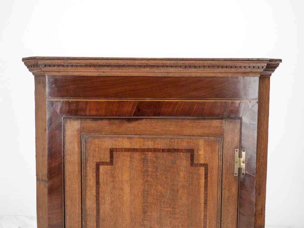 A late 18th-century Georgian oak wall-hanging corner cupboard featuring mahogany crossbanding, an inlaid central lozenge motif, a moulded top cornice, and brass H-hinges. View IX