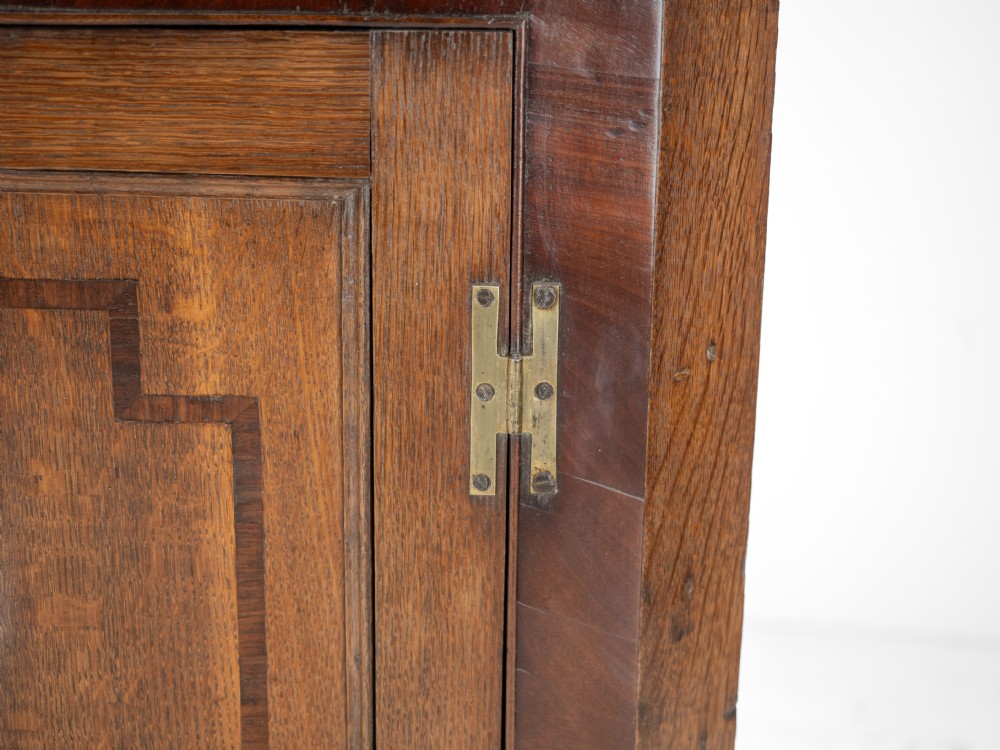 A late 18th-century Georgian oak wall-hanging corner cupboard featuring mahogany crossbanding, an inlaid central lozenge motif, a moulded top cornice, and brass H-hinges. View X