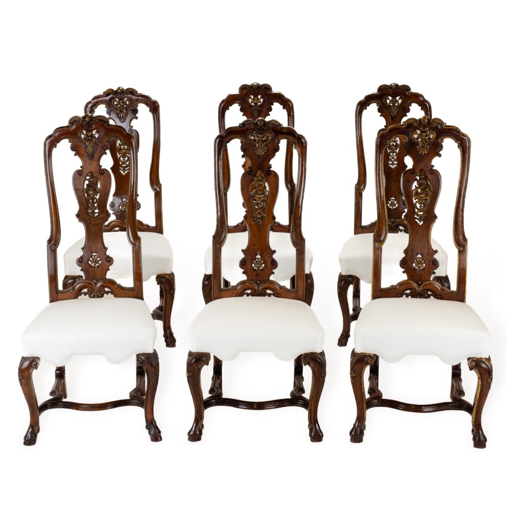 A set of six tall carved walnut dining chairs featuring gilt highlights, pierced splats, and white fabric drop-in seats.
