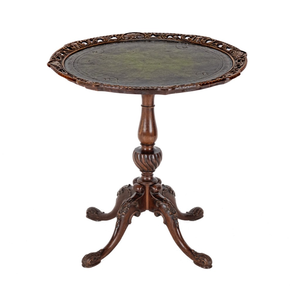 A Chippendale Revival mahogany wine table featuring a green leather top, a piecrust border, a carved central pedestal, and a carved tripod base.