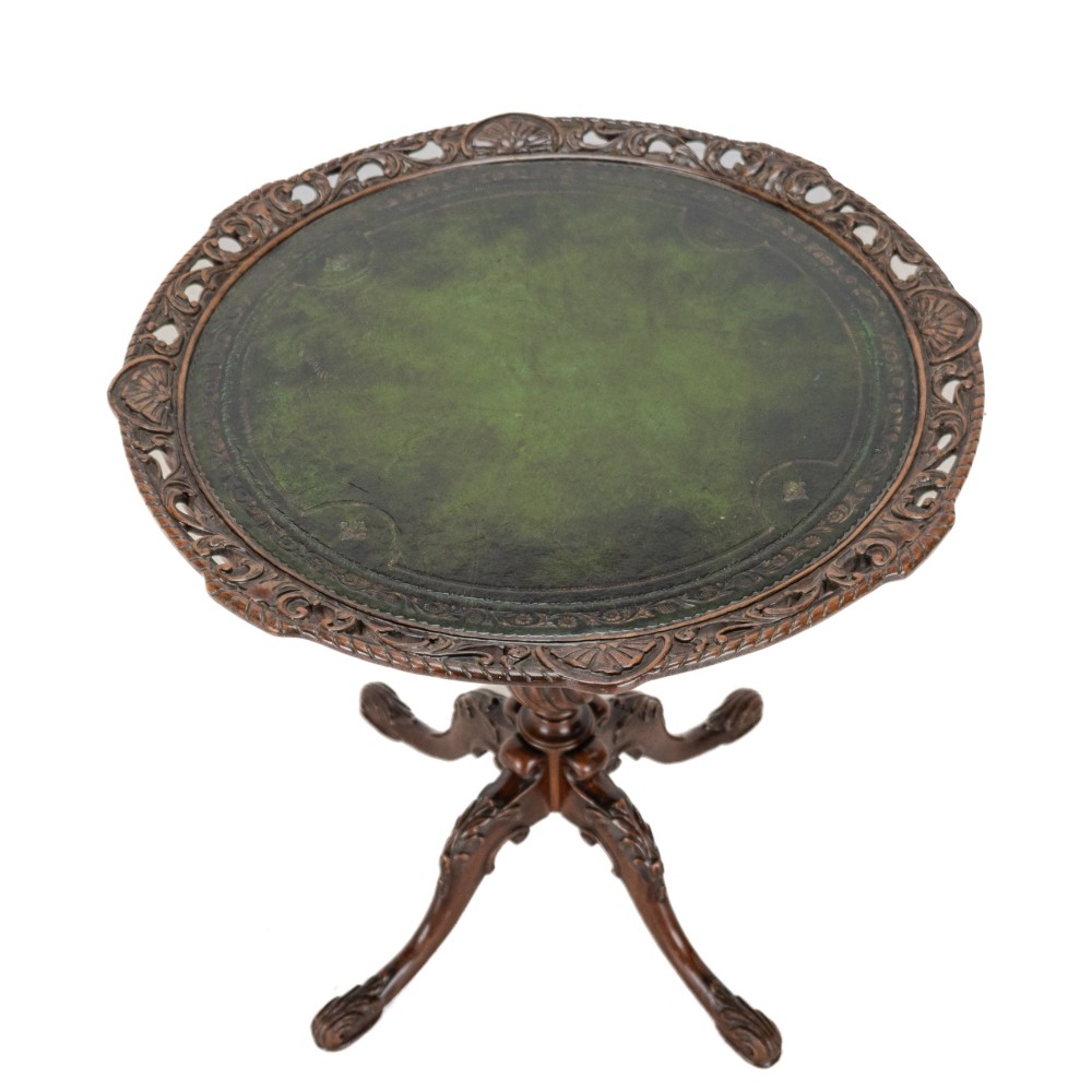 A Chippendale Revival mahogany wine table featuring a green leather top, a piecrust border, a carved central pedestal, and a carved tripod base. View VI