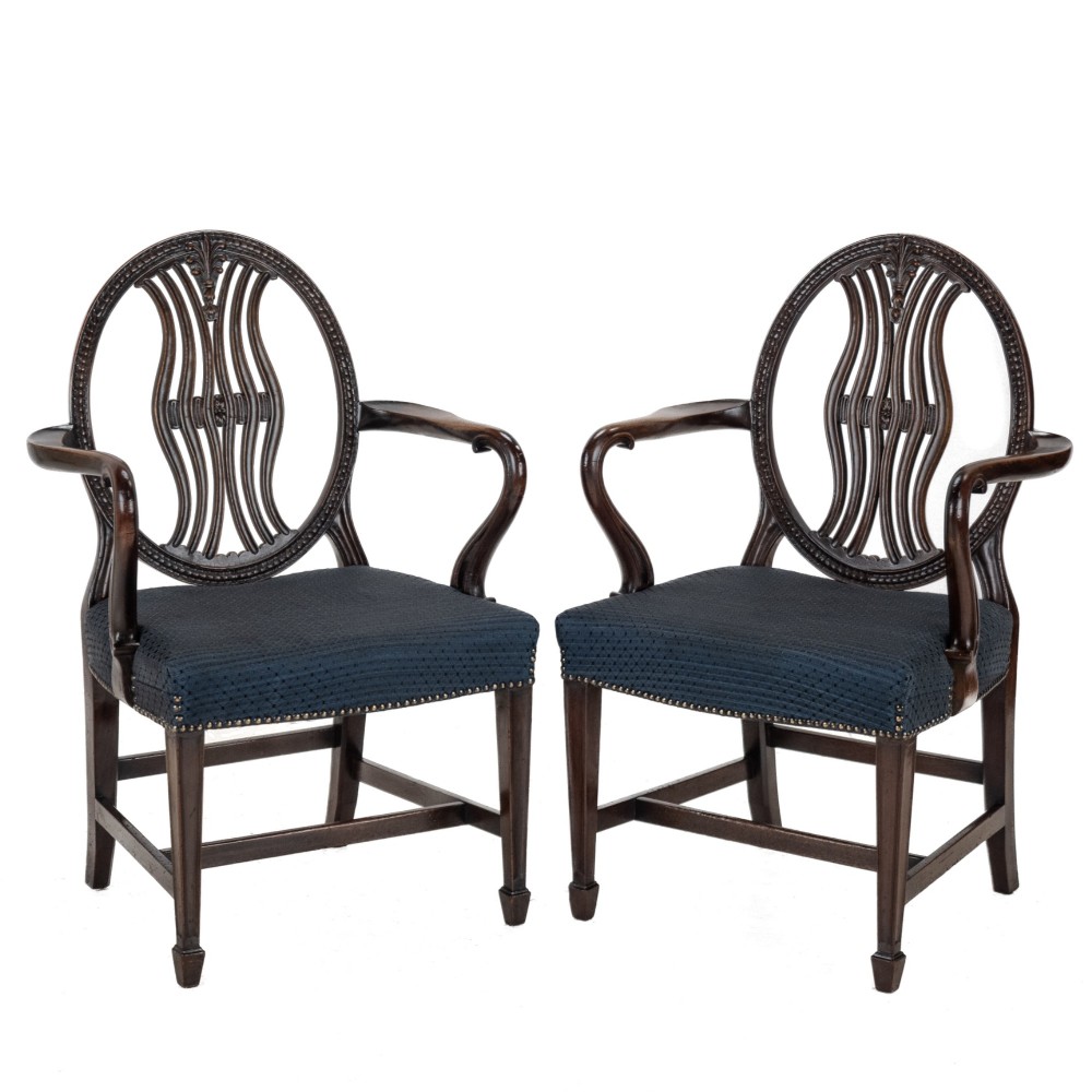 A pair of late 19th-century mahogany Hepplewhite-style carver armchairs featuring carved oval backs and navy blue upholstered seats with brass studding.