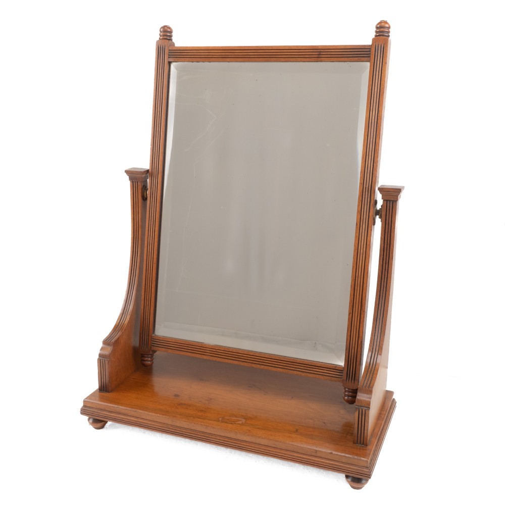 A late 19th-century mahogany table top dressing mirror featuring fluted upright columns, finials, a bevelled rectangular mirror plate, and a moulded wooden base on bun feet.