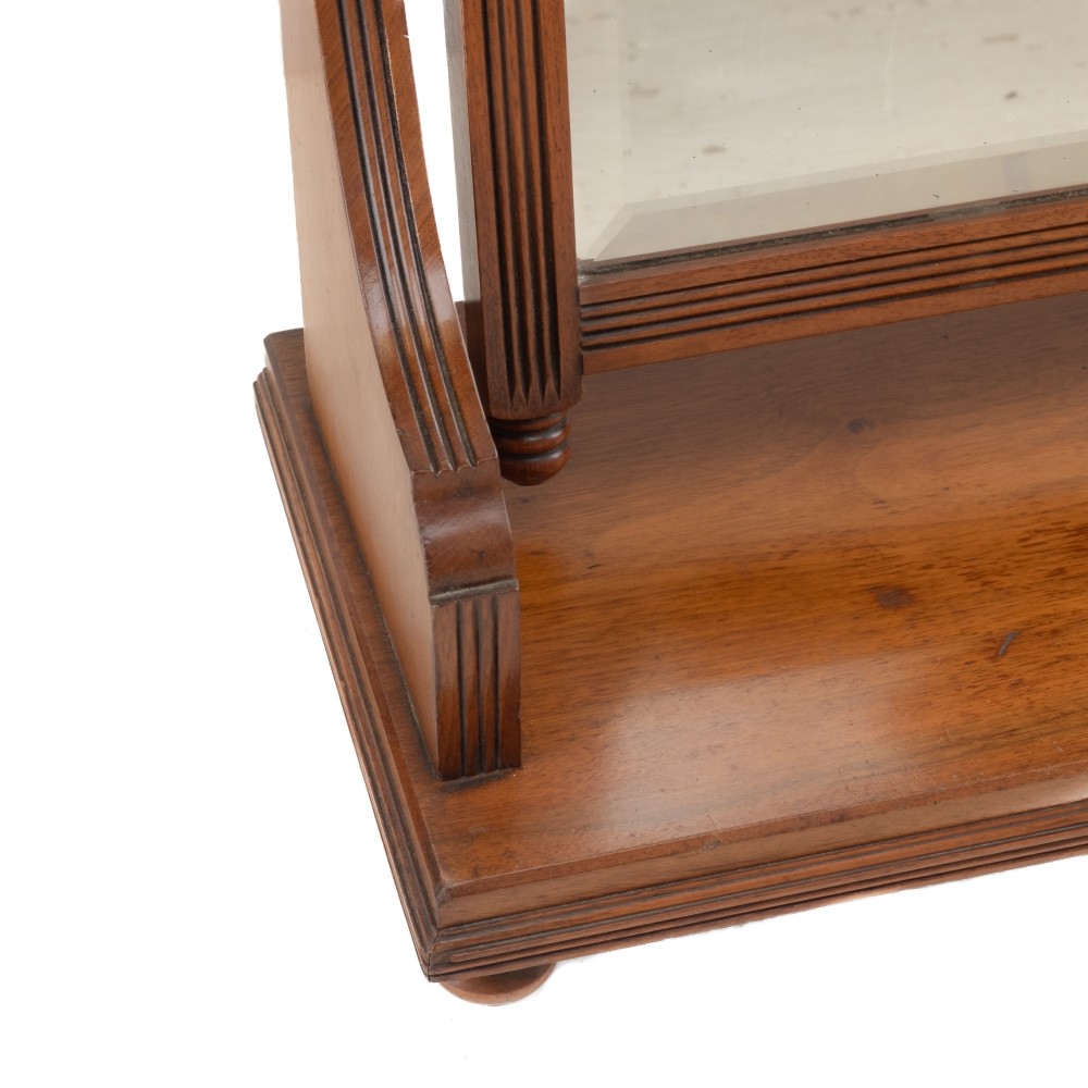 A late 19th-century mahogany table top dressing mirror featuring fluted upright columns, finials, a bevelled rectangular mirror plate, and a moulded wooden base on bun feet. View VI