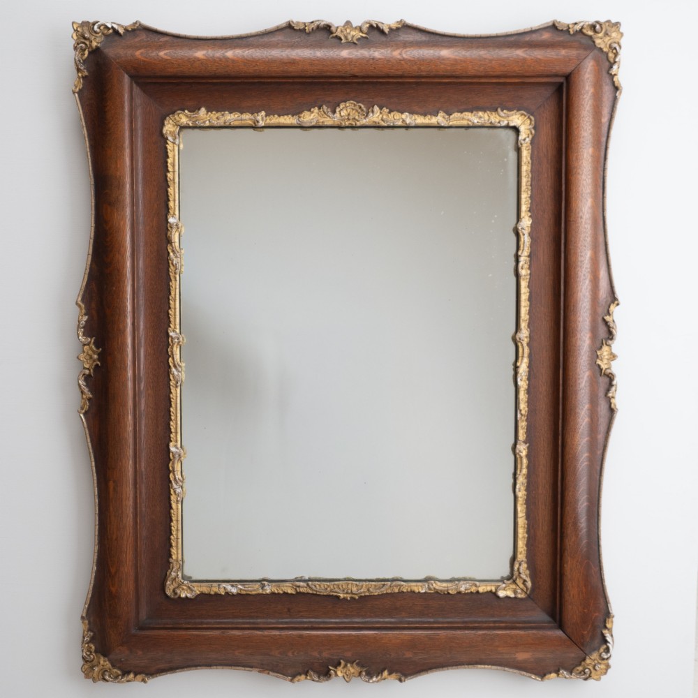 A rectangular dark oak wall mirror featuring a moulded timber frame with gilded gesso accents at the corners, outer edges, and inner sight edge.