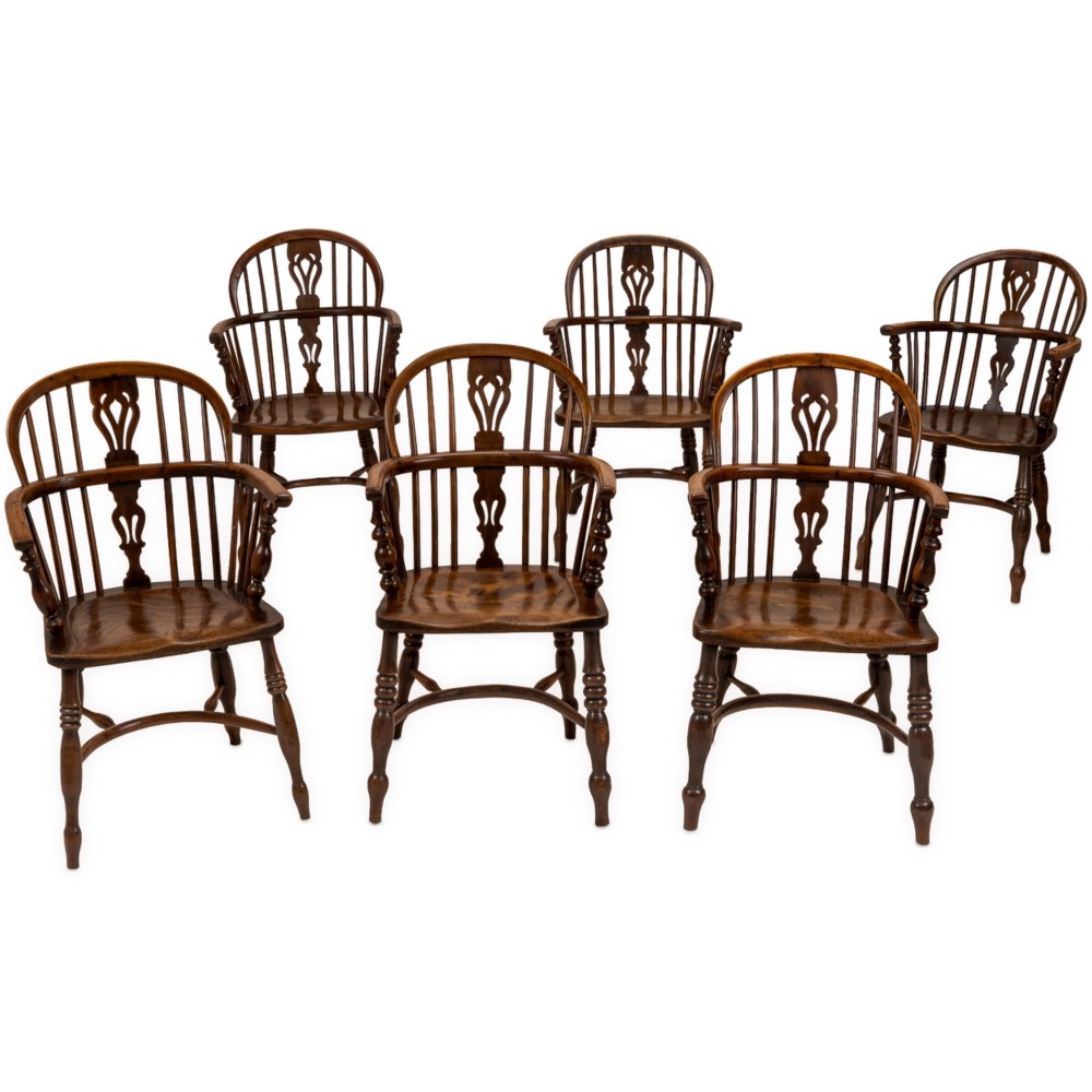 A set of six early 19th-century Windsor armchairs featuring hoop backs, pierced central splats, saddle seats, turned legs, and curved crinoline stretchers.