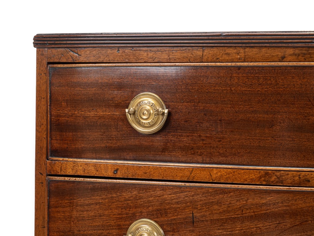 A Regency mahogany bow-front chest of drawers featuring four graduated drawers with circular brass ring handles and splayed bracket feet. View IV