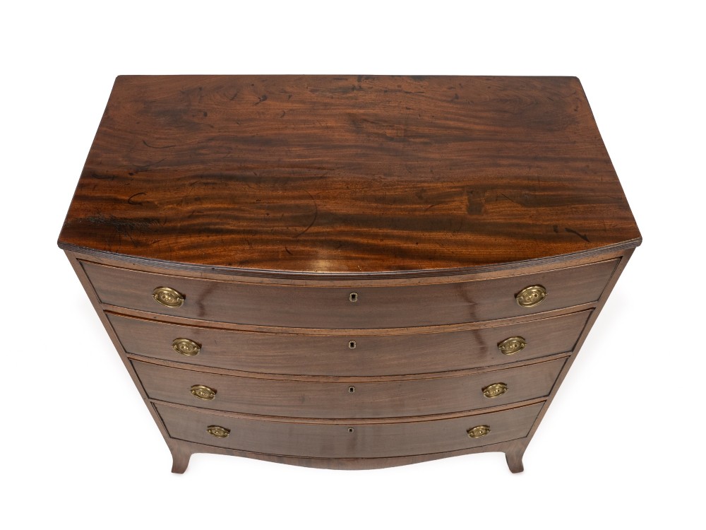 A Regency mahogany bow-front chest of drawers featuring four graduated drawers with circular brass ring handles and splayed bracket feet. View V