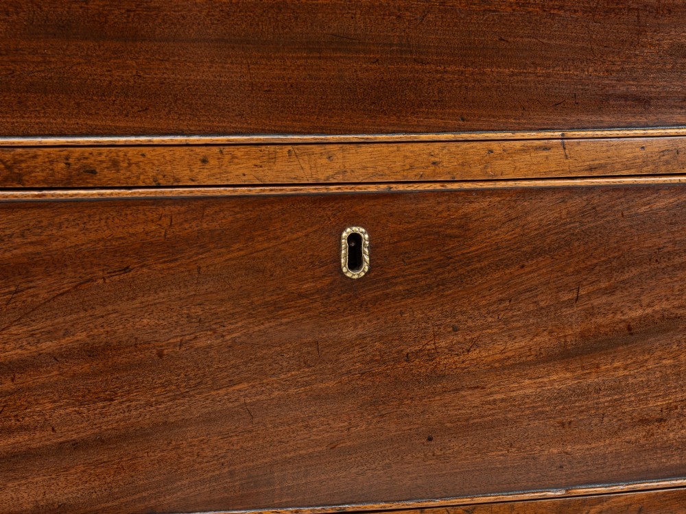A Regency mahogany bow-front chest of drawers featuring four graduated drawers with circular brass ring handles and splayed bracket feet. View VI