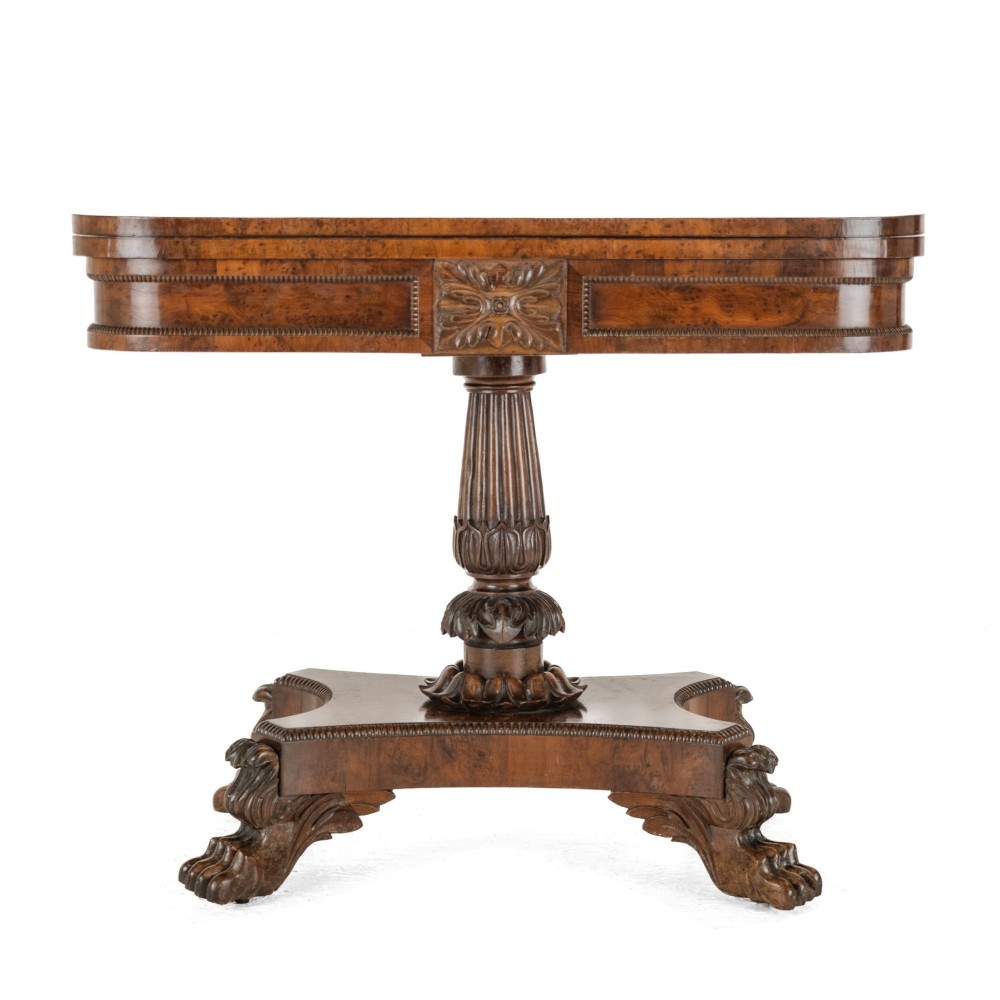 An antique William IV burr yew wood card table with a fold-over top, central carved pedestal column, and paw feet.
