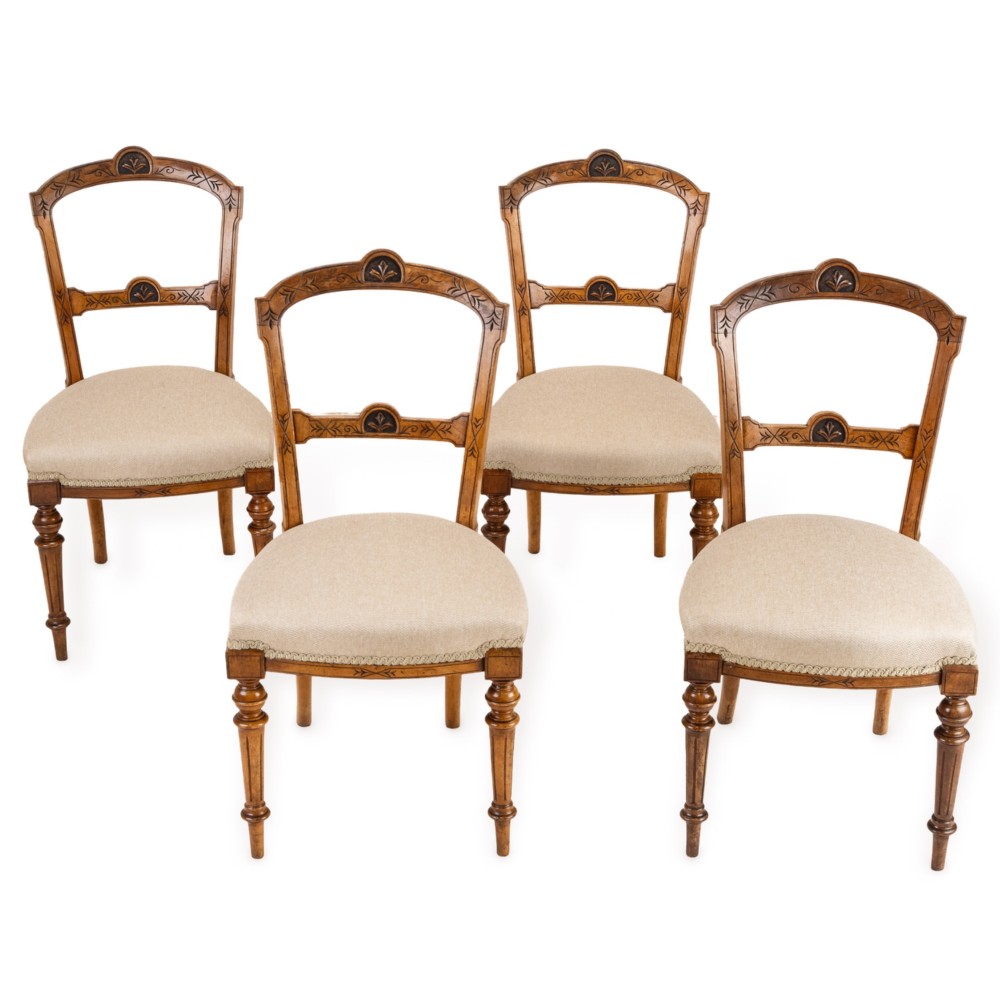 A set of four antique Regency satin birch dining chairs featuring carved crest rails, turned front legs, and neutral fabric upholstered seats.